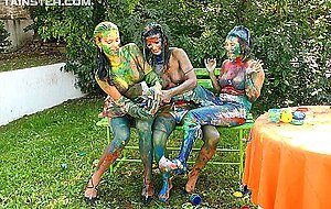 Clothed women cover themselves in finger paint on a garden bench